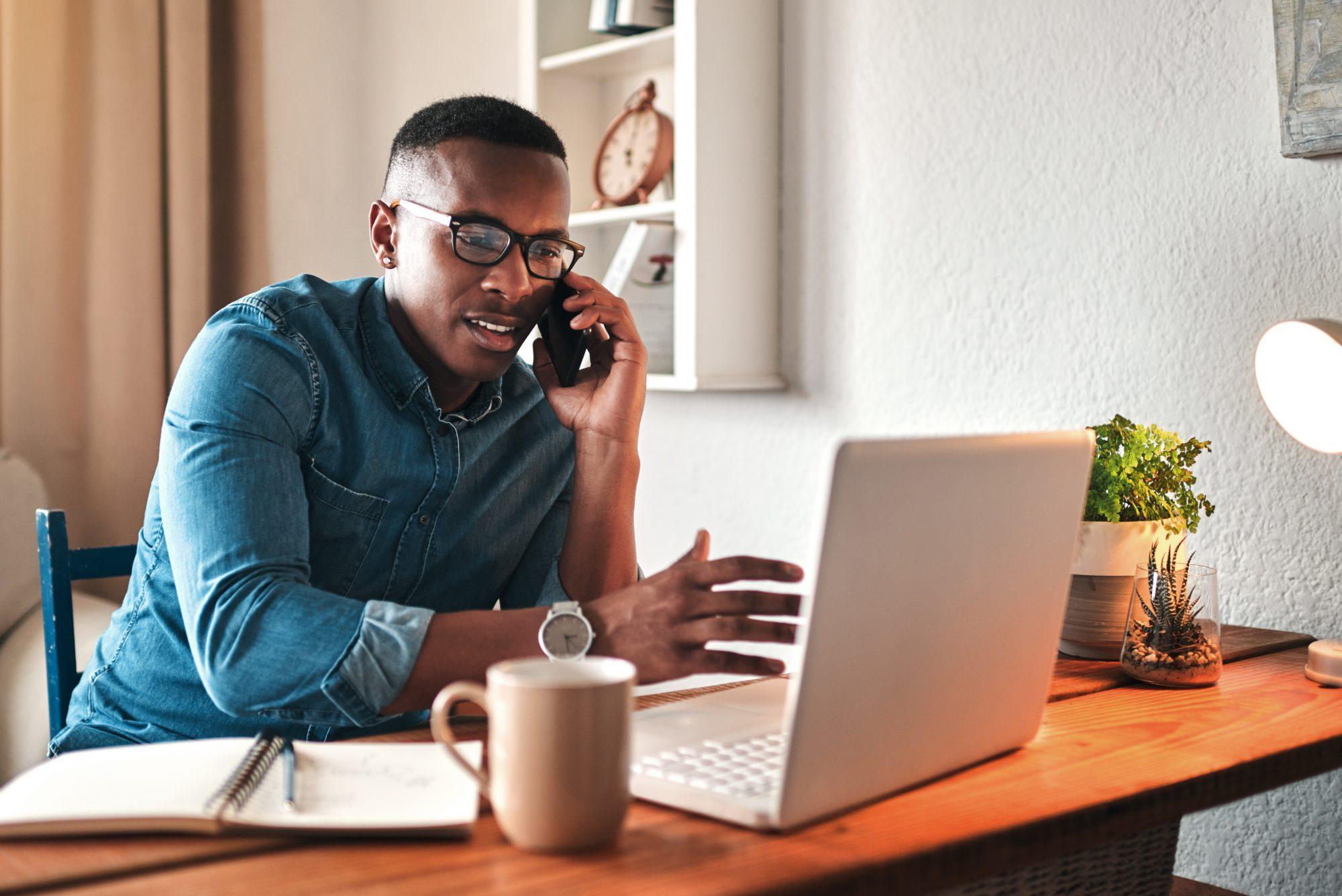 young businessman sitting alone in his home office and talking on his cellphone