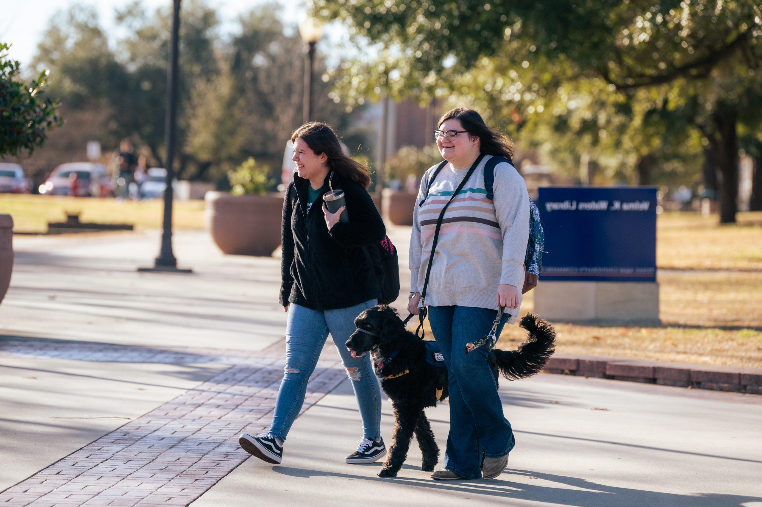 Two female students walking with one who has a service dog.